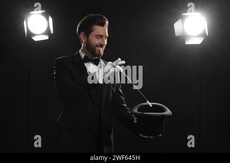 Happy magician showing magic trick with top hat on stage Stock Photo