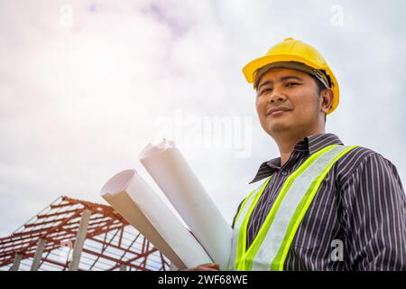 Asian business man construction engineer worker in protective helmet and blueprints paper on hand at building site Stock Photo