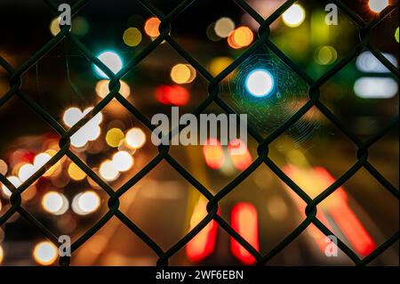 Close-up view of a chain-link fence with a mesmerizing bokeh effect of city lights blurred in the night-time background. Stock Photo