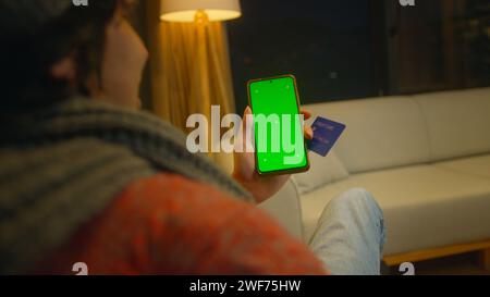 Man holding credit card, using, tapping on screen smartphone with green mock-up screen. Close-up over the shoulder shot Stock Photo