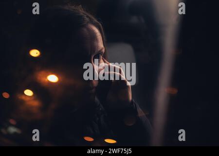 Woman talking on mobile phone from the car back seat at night, seen through the window from the outside of the vehicle, selective focus Stock Photo
