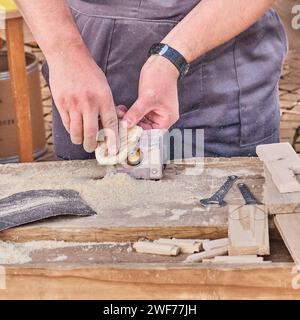 Male hands sanding edges of wooden little heart using small electric machine tool. Stock Photo