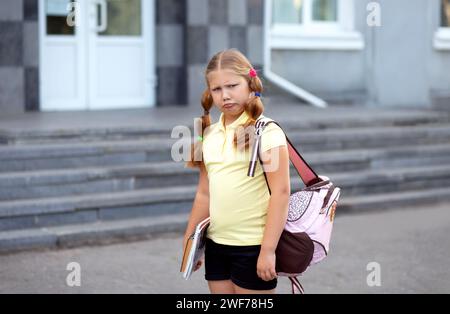 Pretty schoolgirl offended upset sad angry after lessons on the doorstep of the school. Tired student - hard school day Stock Photo