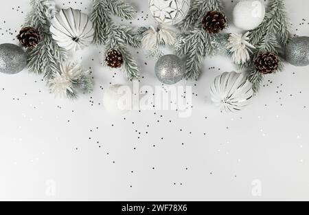 Christmas composition, white and silver decorations, fir tree branches, pinecones, silver stars confetti on white background. Stock Photo