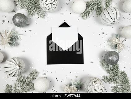 Christmas composition, black envelope, white and silver decorations, fir tree branches, silver stars confetti on white background. Stock Photo