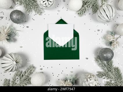 Christmas composition, green envelope, white and silver decorations, fir tree branches, silver stars confetti on white background. Stock Photo