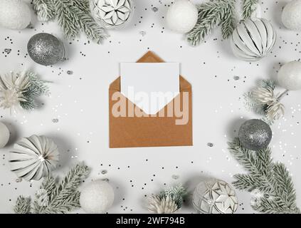 Christmas composition, kraft envelope, white and silver decorations, fir tree branches, silver stars confetti on white background. Stock Photo
