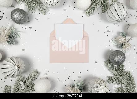 Christmas composition, pink envelope, white and silver decorations, fir tree branches, silver stars confetti on white background. Stock Photo