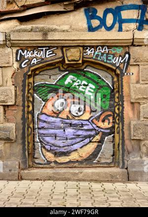 Boy with face mask graffiti street art with Cyrillic text reading Masks are for protection in Sofia, Bulgaria, Eastern Europe, Balkans, EU Stock Photo