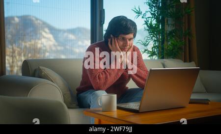 College student working from home using with laptop while sitting on sofa in living room. Bored man student trying to study, staring blankly at the sc Stock Photo