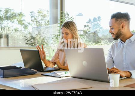 Two business people working on their laptops while sitting on a desk at the office. Business concept. Stock Photo