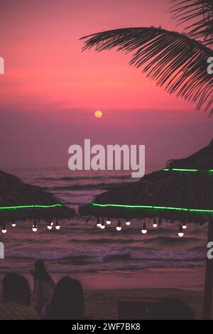 Beach huts on empty beach at twilight, surrounded by palm trees and vibrant greenery: Sunset, Da Nang, Vietnam Stock Photo