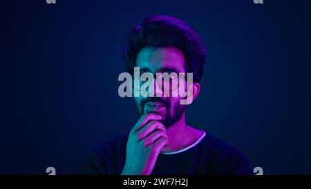 Close up male portrait in neon studio ultraviolet background blue backdrop Arabian Muslim shocked amazed guy astonish wonder excited Indian man Stock Photo