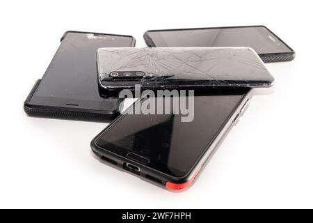 Pile of broken smartphones isolated on white background. Damaged mobile phones with cracked screen. Stock Photo