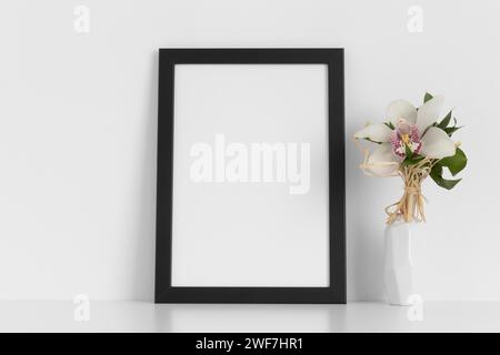 Black frame mockup with a orchid on the white table. Stock Photo
