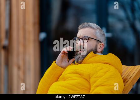 Portrait of handsome man phone calling from patio, during cold winter day. Handsome man spending relaxing winter weekend in cabin in mountains Stock Photo