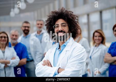 Portrait of handsome doctor standing in front of team of doctors. Healthcare team with doctors, nurses, professionals in medical uniforms in hospital. Stock Photo