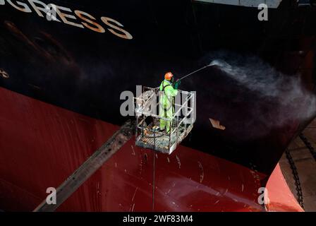 High angle image of a dock worker steam cleaning the hull of a tanker in dry dock. Stock Photo