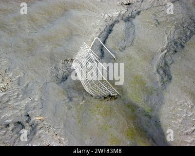 An abandoned supermarket basket in the mud of a river estuary Stock Photo