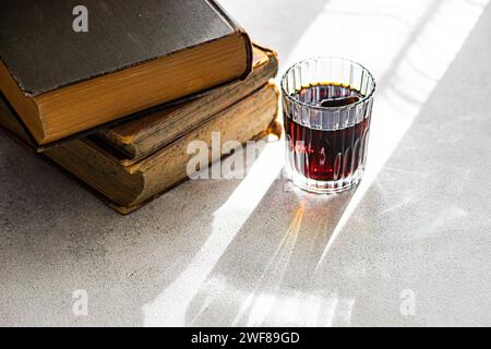 Cherry liqueur in a clear glass beside a stack of vintage books on a sunlit surface Stock Photo