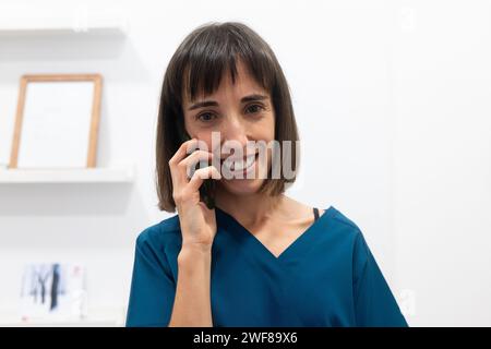 A happy woman dressed in a stylish blue top speaks on a mobile phone in a bright interior setting Stock Photo