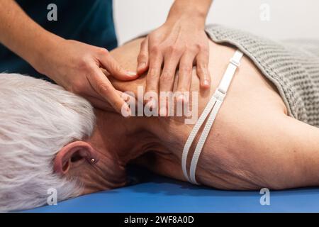 A close-up image depicting a physiotherapist’s hands applying treatment to an elderly patient's shoulder Stock Photo