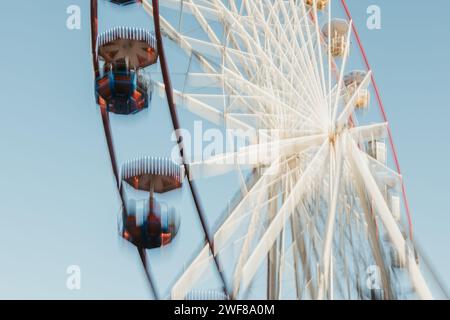 From below dynamic, motion-blurred Ferris wheel with a sense of speed and movement under a bright blue sky Stock Photo