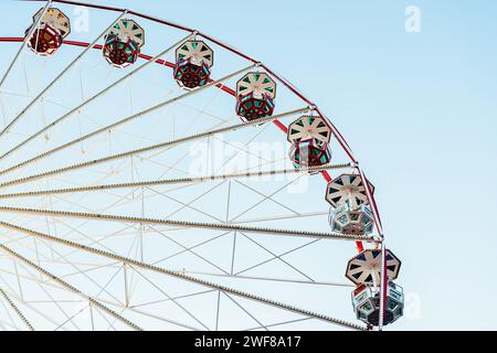 From below static Ferris wheel against a clear blue sky, showcasing its symmetry and colorful patterns on the passenger cabins Stock Photo