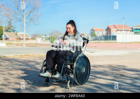 A young woman in a wheelchair is using her smartphone in a sunny park Stock Photo
