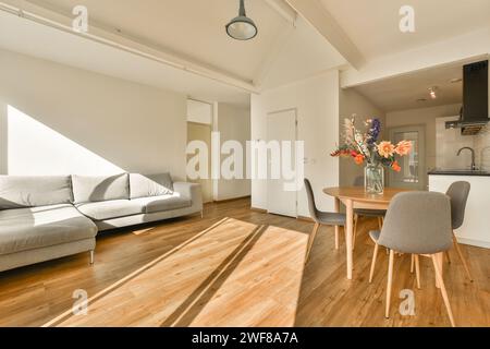 A cozy and stylish living room with a large gray sofa, wooden floors, and a dining area bathed in sunlight. Stock Photo