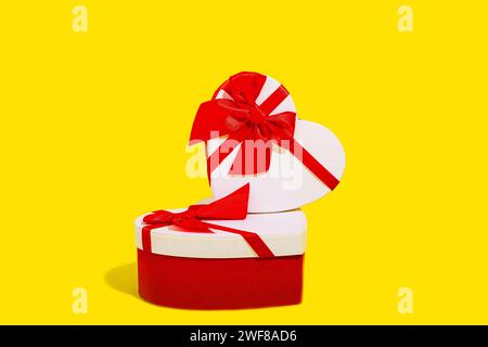 A stacked arrangement of two heart shaped gift boxes with vibrant red ribbons on a yellow background Stock Photo