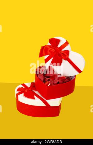 Open heart-shaped gift box with red ribbons on top of a closed one against a yellow backdrop Stock Photo