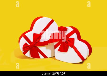 Two white heart-shaped gift boxes with red ribbons on a yellow background Stock Photo
