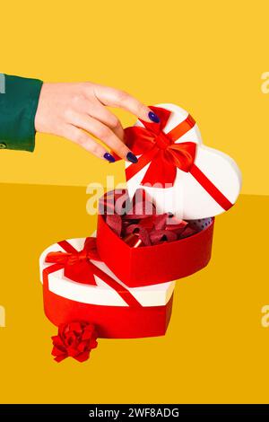 Anonymous hand opening a heart-shaped gift box with red ribbons on a yellow background Stock Photo