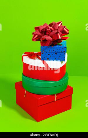 A colorful stack of various shaped gift boxes with a glittering bow on a bright green background Stock Photo