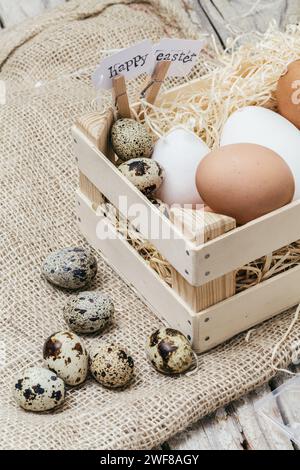 A wooden basket filled with various eggs and a sign reading 'Happy Easter' on rustic burlap. Stock Photo