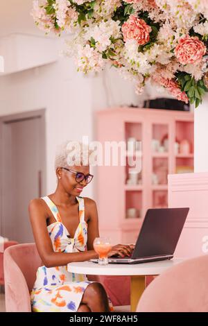 Young woman in casual clothes and glasses sitting at table with laptop and looking at screen Stock Photo