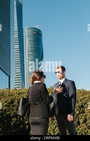 Two business professionals engage in a discussion with modern skyscrapers of Madrid in the background. Stock Photo