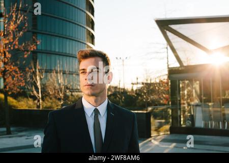 A young professional in a sharp suit stands confidently in Madrid, with the setting sun casting a warm glow. Stock Photo