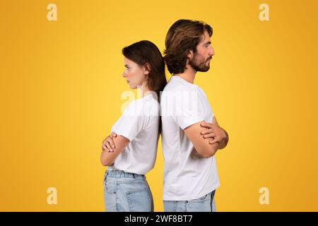 A couple in white t-shirts and blue jeans stands back to back with crossed arms Stock Photo