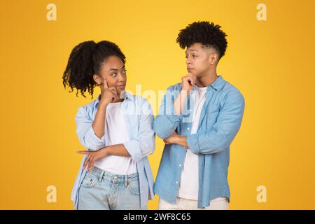 Thoughtful young African American woman and man with hands on chin, looking at each other Stock Photo