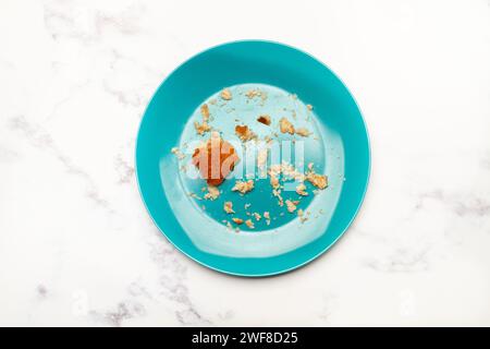 A blue plate with a piece of bread and breadcrumbs on a marble kitchen counter in a top view Stock Photo