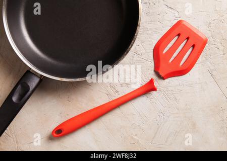 Broken red spatula with a frying pan on a textured background Stock Photo