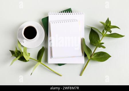 Composition with opened blank notepad, cup of black coffee, green leaves on a gray background. Hello spring. Morning coffee cup. Stock Photo