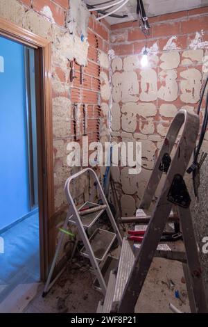 A room under renovation with chipped walls, debris on the floor, construction tools, ladders, and a single bulb hanging from the ceiling. Home renovat Stock Photo