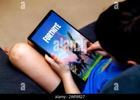 Fortnite game app on tablet screen in kid's hands close-up. Little boy playing on a tablet, on the couch at home. It is a very popular game. Rosario, Stock Photo