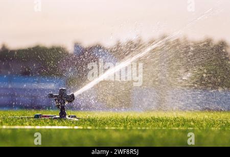 Automatic lawn sprinkler watering green grass on sunny summer days ...
