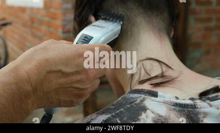 a man cuts a teenager's hair using an electric clipper, view from the back, close-up, home hair care and men's haircut Stock Photo