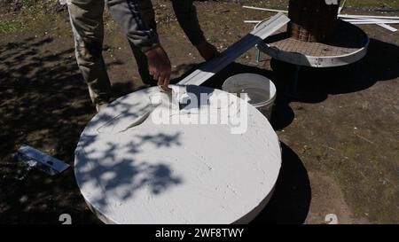 covering a round tabletop with plaster in the process of making original furniture using mortar and spatulas, the master spreads the mixture Stock Photo