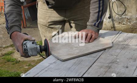 processing the edge of the tile with emery on a miter saw on an outdoor work surface, cutting and leveling a piece of tile of a certain shape Stock Photo